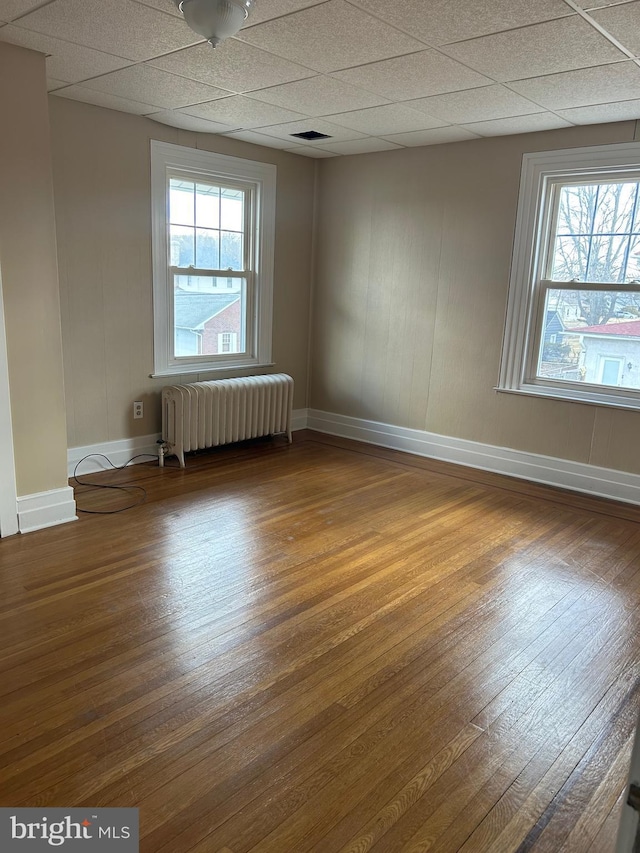 spare room with radiator, a drop ceiling, wood-type flooring, and baseboards