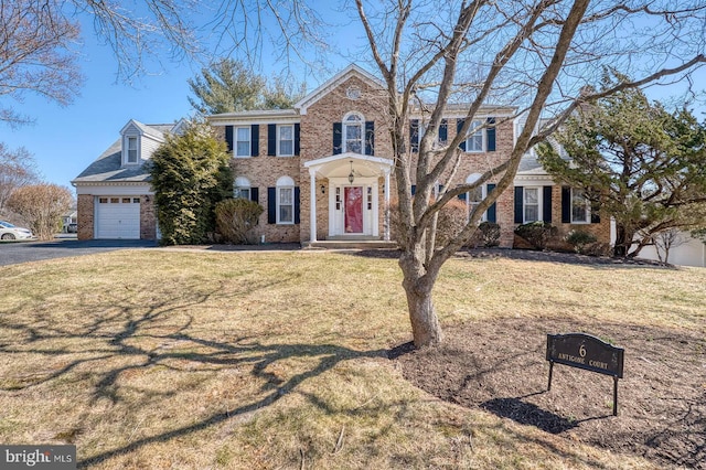 colonial house featuring a garage, driveway, brick siding, and a front yard