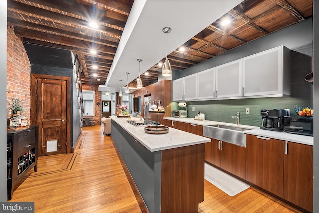 kitchen with black microwave, light wood-style flooring, a kitchen island, a sink, and white cabinets