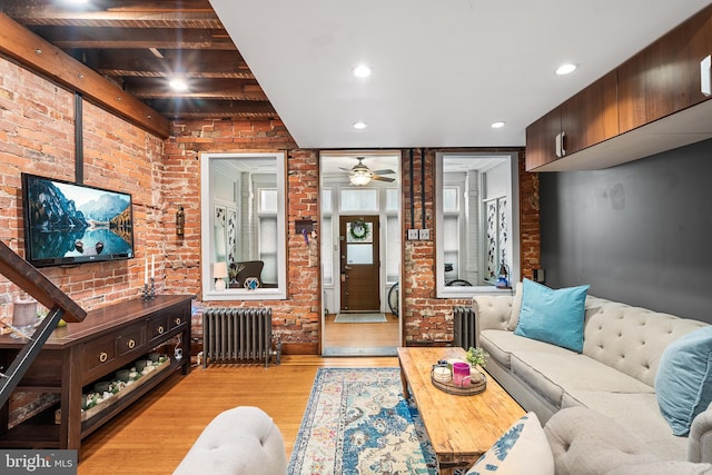 living room featuring a ceiling fan, radiator, light wood finished floors, and brick wall