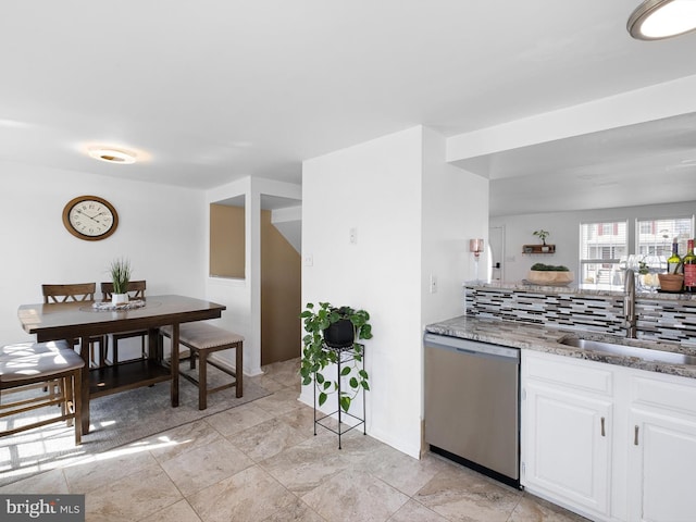 kitchen with tasteful backsplash, light stone countertops, dishwasher, white cabinets, and a sink