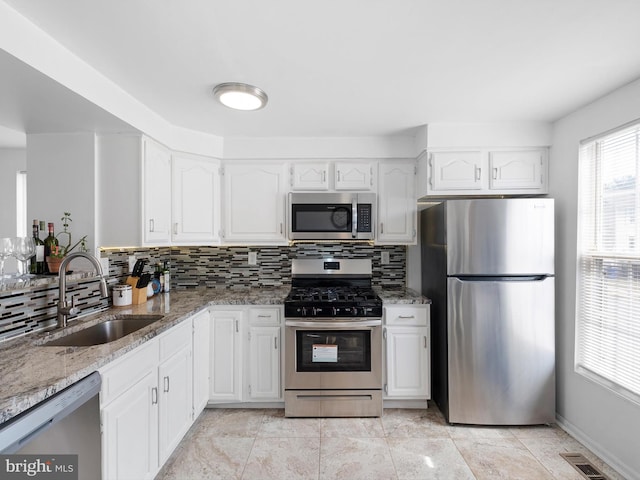 kitchen featuring visible vents, a sink, appliances with stainless steel finishes, decorative backsplash, and light stone countertops