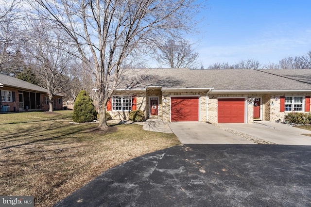 ranch-style house with roof with shingles, brick siding, an attached garage, a front yard, and driveway