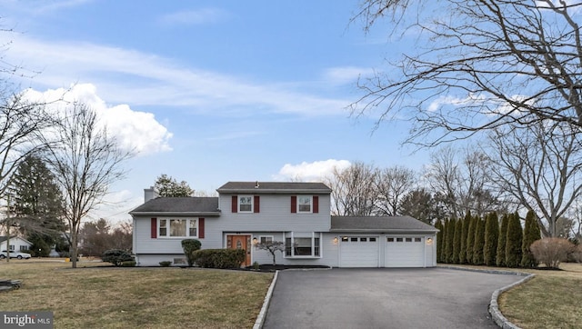 split level home with an attached garage, aphalt driveway, a chimney, and a front lawn