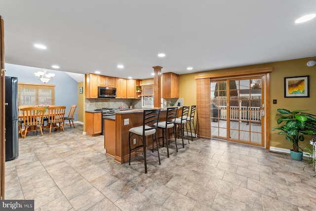 kitchen with tasteful backsplash, stainless steel microwave, a breakfast bar area, freestanding refrigerator, and a peninsula