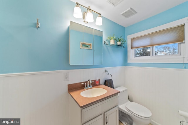 bathroom featuring a wainscoted wall, visible vents, vanity, and toilet