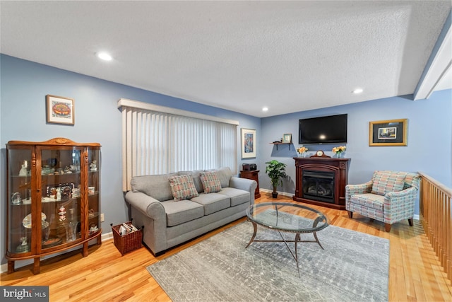 living room featuring a textured ceiling, a fireplace, baseboards, and wood finished floors