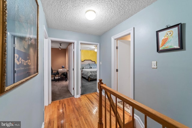 hallway featuring a textured ceiling, light wood finished floors, and an upstairs landing