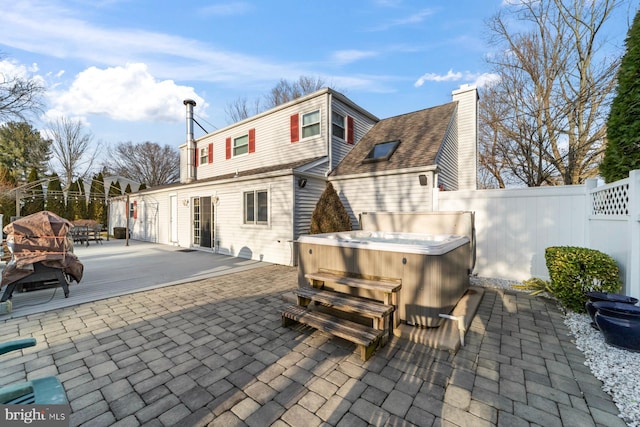 back of property featuring a patio, a chimney, fence, and a hot tub