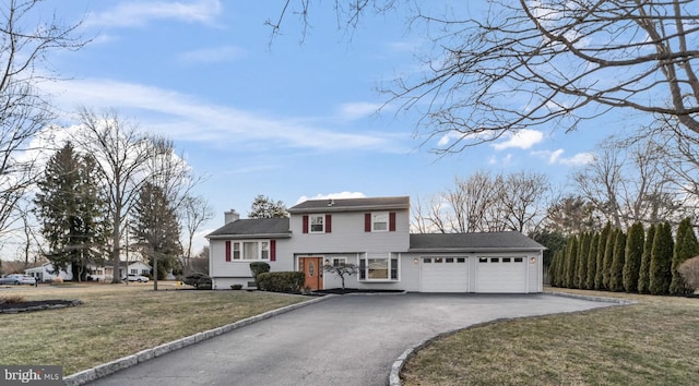 view of front of house with an attached garage, a chimney, a front lawn, and aphalt driveway