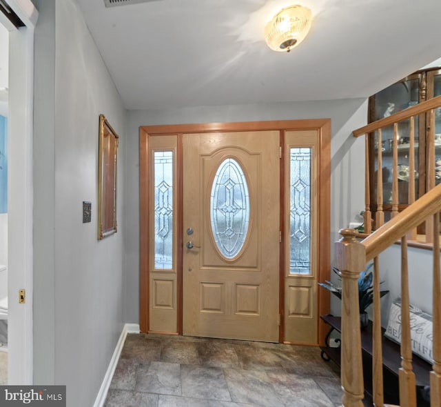 foyer entrance featuring stone finish floor, stairway, and baseboards