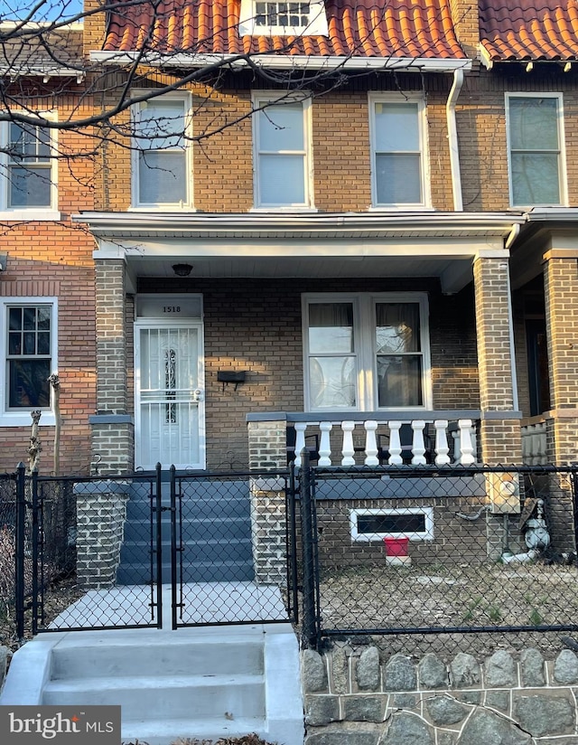 view of exterior entry featuring brick siding, a tiled roof, a porch, and a gate