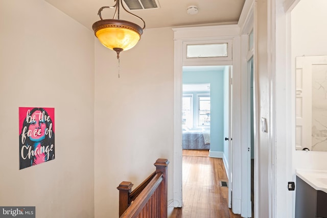 corridor featuring hardwood / wood-style flooring, visible vents, and an upstairs landing