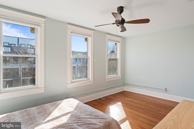 bedroom featuring multiple windows, ceiling fan, baseboards, and wood finished floors