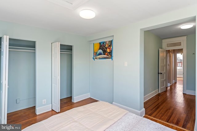 bedroom featuring multiple closets, baseboards, and wood finished floors