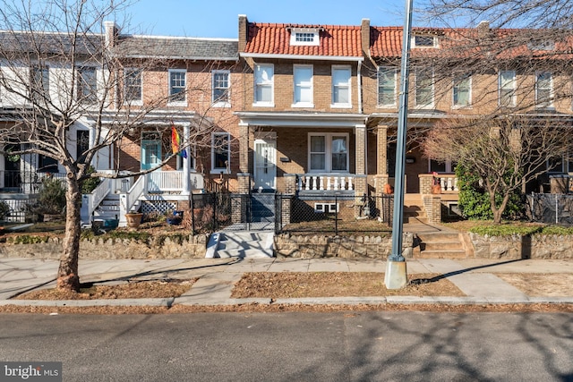 multi unit property with covered porch, a tile roof, a fenced front yard, and brick siding