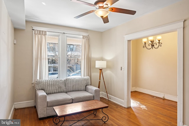 sitting room with ceiling fan with notable chandelier, baseboards, and wood finished floors