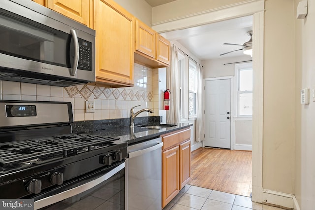 kitchen with dark stone counters, ceiling fan, appliances with stainless steel finishes, a sink, and backsplash