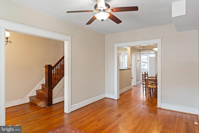 spare room with light wood-style floors, stairway, baseboards, and a ceiling fan