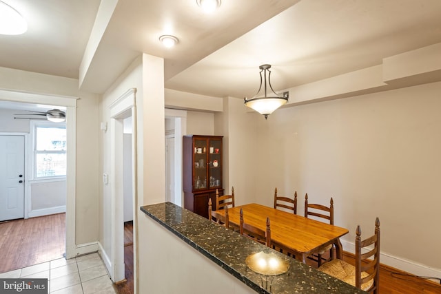 kitchen featuring light tile patterned floors, baseboards, pendant lighting, and dark stone countertops