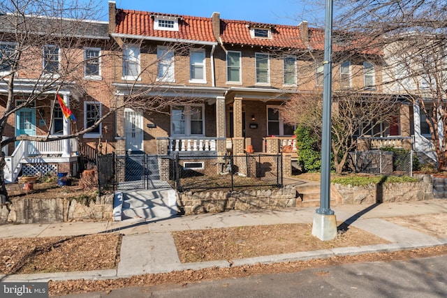 view of property featuring a fenced front yard, a tile roof, brick siding, a porch, and a gate