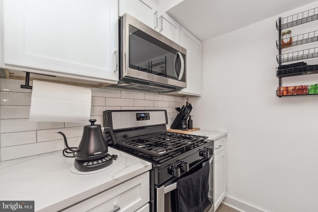 kitchen with stainless steel appliances, decorative backsplash, white cabinets, light stone countertops, and baseboards