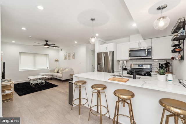 kitchen featuring stainless steel appliances, a peninsula, a sink, white cabinetry, and decorative light fixtures