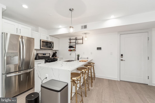 kitchen with visible vents, a breakfast bar area, stainless steel appliances, light wood-style floors, and a sink