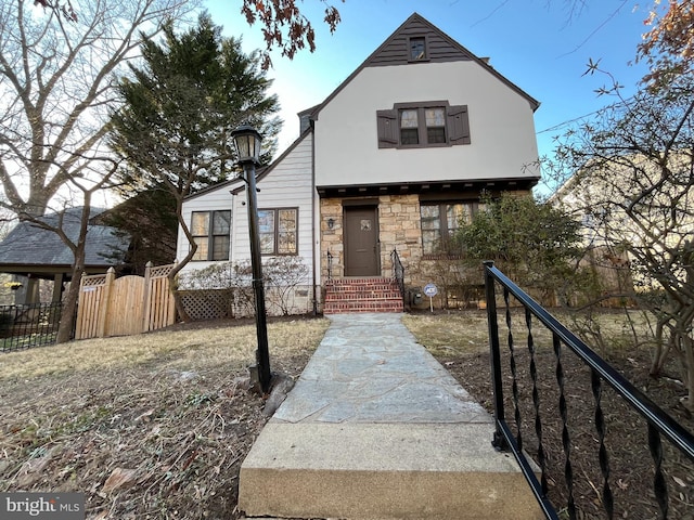 view of front of house featuring fence, stone siding, and stucco siding