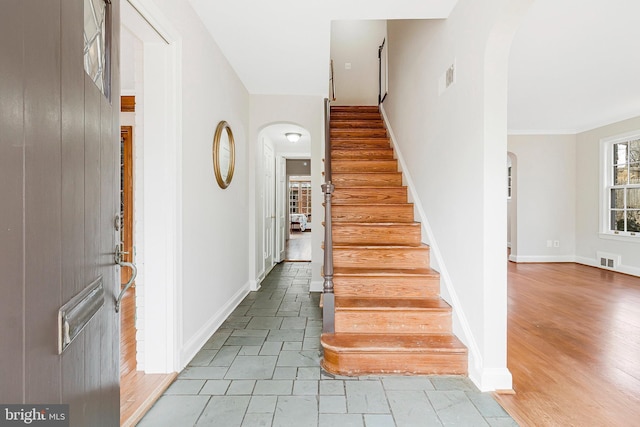 stairs with arched walkways, visible vents, baseboards, and wood finished floors