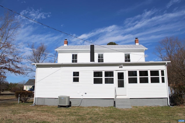 rear view of house featuring metal roof, a lawn, a chimney, and central AC unit