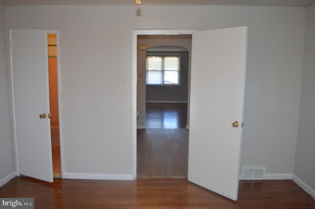 spare room featuring arched walkways, visible vents, baseboards, and wood finished floors