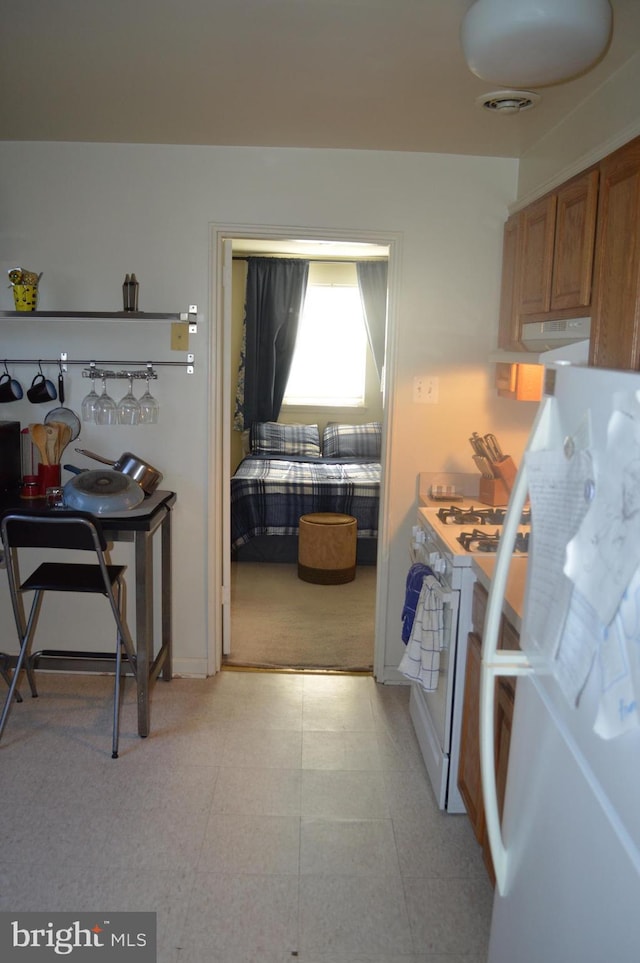 kitchen with white appliances, baseboards, visible vents, brown cabinetry, and exhaust hood