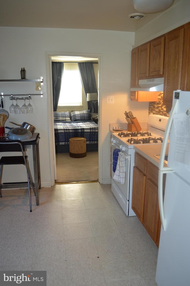 kitchen with light countertops, visible vents, brown cabinetry, white appliances, and under cabinet range hood