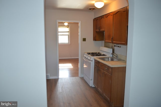 kitchen featuring light countertops, brown cabinetry, white range with gas cooktop, a sink, and wood finished floors