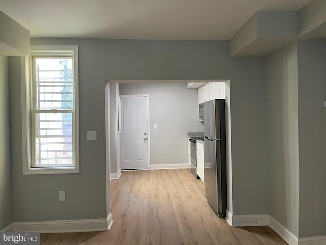 interior space featuring white cabinetry, baseboards, light wood-type flooring, freestanding refrigerator, and electric range oven