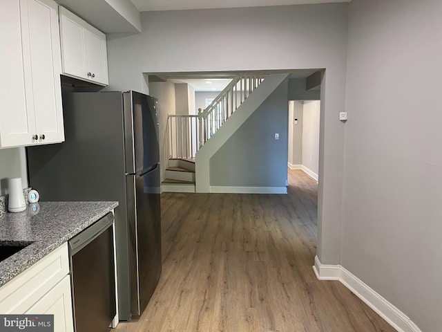 kitchen featuring light wood finished floors, baseboards, white cabinets, dishwasher, and light stone counters