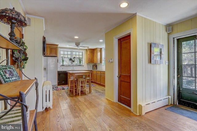 kitchen with light wood finished floors, white refrigerator with ice dispenser, a center island, crown molding, and a baseboard heating unit