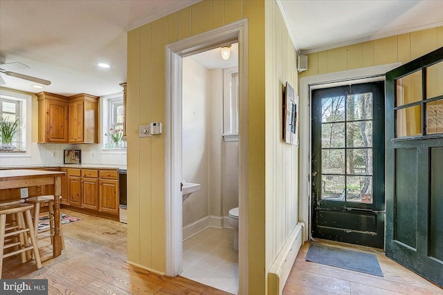 doorway to outside with ornamental molding, a wealth of natural light, and light wood finished floors