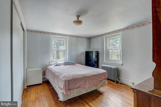 bedroom featuring multiple windows, radiator heating unit, wood-type flooring, and baseboards