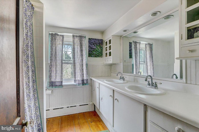 full bathroom featuring double vanity, a sink, baseboard heating, and wood finished floors