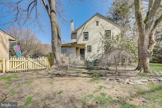 back of house with a chimney, fence, and a gate