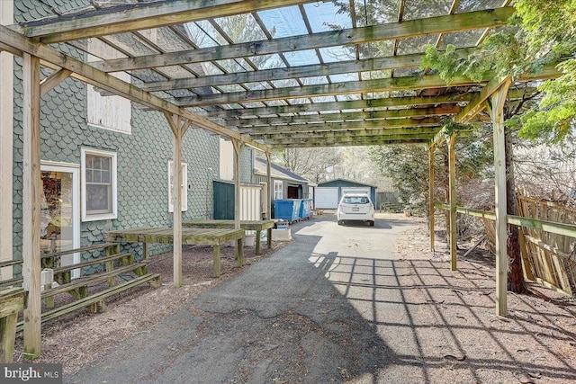 view of patio / terrace with a pergola, aphalt driveway, a carport, and an outbuilding