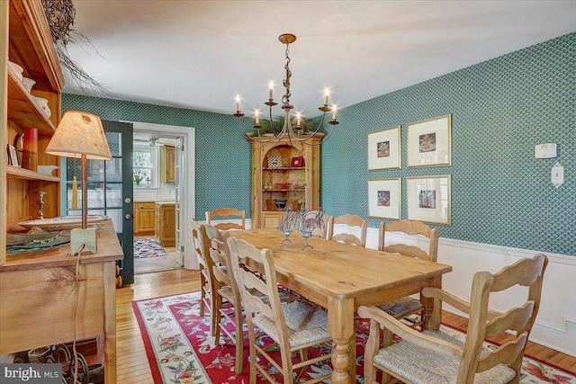 dining area featuring wallpapered walls, light wood-style flooring, a chandelier, and wainscoting