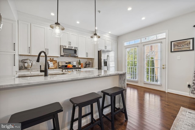 kitchen featuring dark wood-type flooring, a sink, a kitchen breakfast bar, appliances with stainless steel finishes, and decorative backsplash