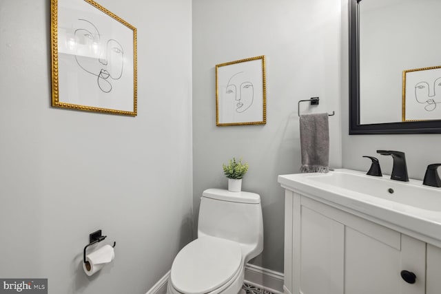 half bathroom featuring toilet, baseboards, and vanity