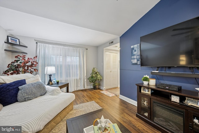 living room with lofted ceiling, wood finished floors, visible vents, and baseboards