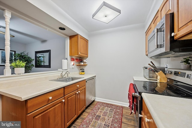 kitchen featuring baseboards, appliances with stainless steel finishes, wood finished floors, light countertops, and a sink