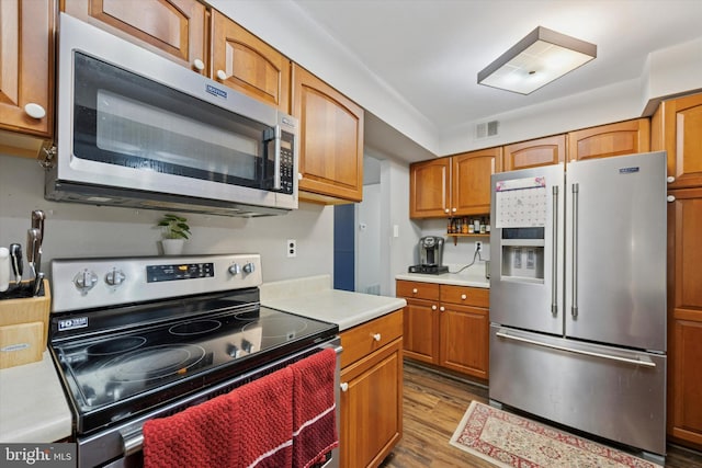 kitchen with visible vents, appliances with stainless steel finishes, brown cabinets, dark wood-style flooring, and light countertops