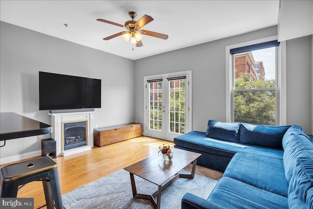 living area featuring french doors, a fireplace, ceiling fan, wood finished floors, and baseboards